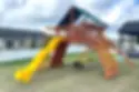 Expansive wooden playset with a BYB tarp, double-wall yellow scoop slide, climbing wall, and a swing set for hours of outdoor fun.