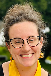 choir director Emily gait-scaglioni smiling wearing glasses, yellow earrings and a yellow scarf