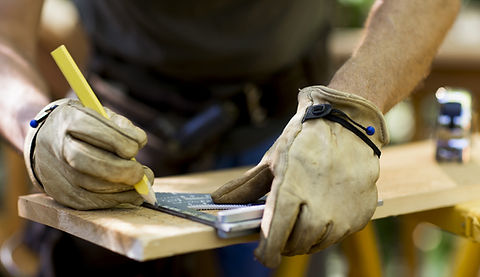 Carpenter wearing leather gloves draws a line on a plank of wood using a set square