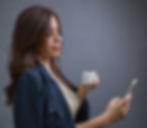 Empresária analisando o celular com expressão séria, segurando uma xícara de café, conceito de tomada de decisão financeira.