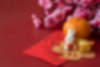 Bunny figurine with fish, gold ingot, orange, pink flowers, and red envelopes on a red background, conveying a festive mood.