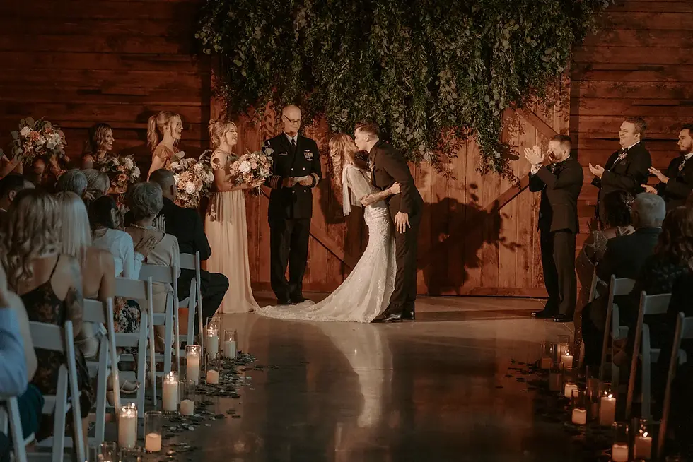 A romantic indoor wedding ceremony inside the historic HayBarn at The Barn at Silverstone, featuring rustic stone walls and lush greenery at the altar.