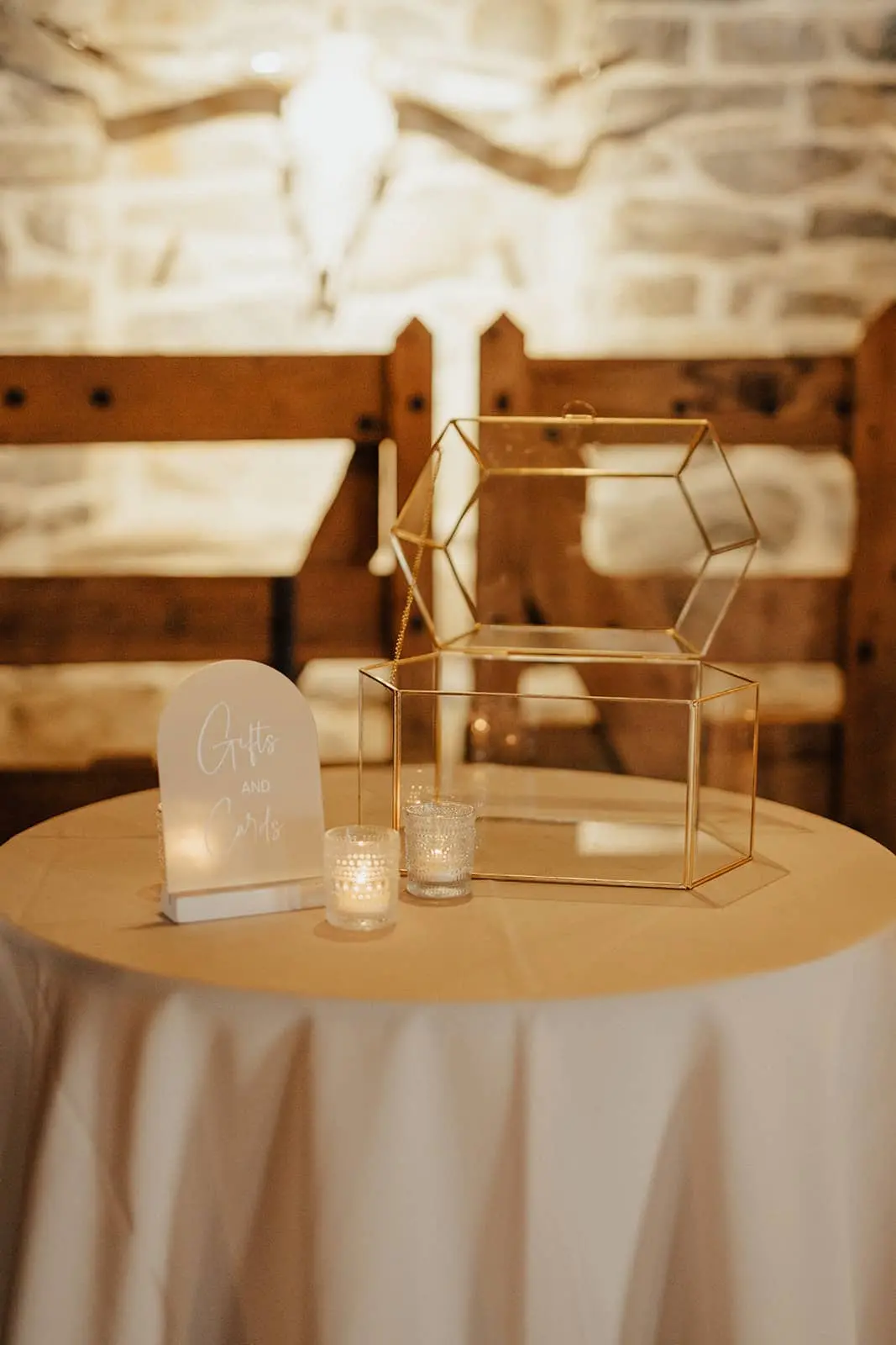 Modern, clear acrylic arched table sign with elegant white typography, surrounded by lit candles on a wooden wedding reception table.