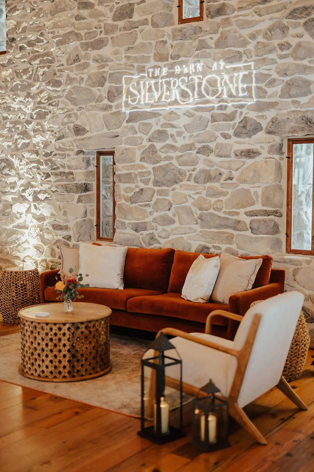 Elegant luxury lounge furniture setup featuring a leather sofa and vintage chairs by a historic stone fireplace at the barn at silverstone luxury wedding venue.