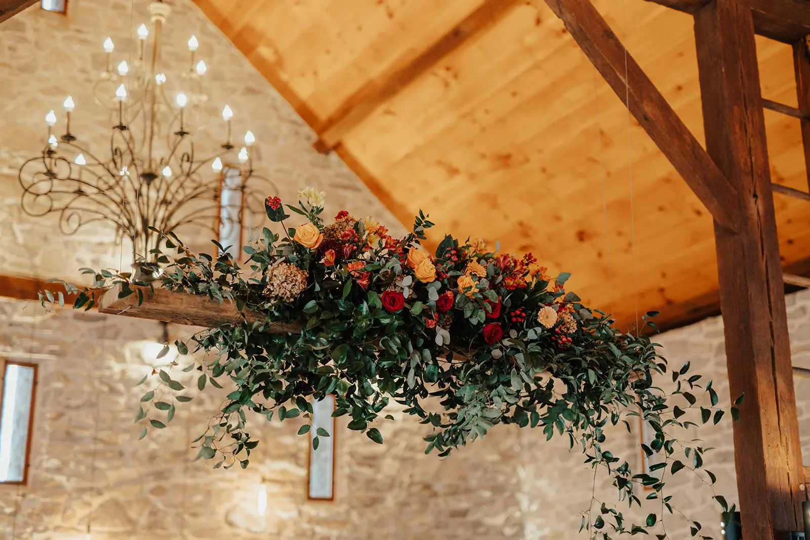 Lush, cascading floral installation featuring white blooms and greenery on a floating grand wooden wooden beam at the barn at silverstone luxury wedding venue.
