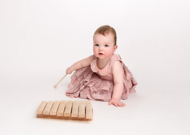 Baby girl in a pretty pink dress plays with a wooden xylophone, portrait by Christchurch Baby Photographer Kirsten Naomi Photography