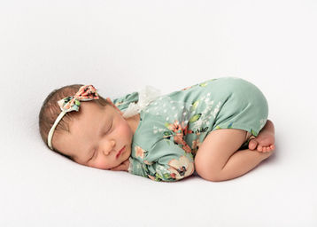 Photograph of a newborn baby girl on her tummy wearing a pretty green floral outfit and matching headband by Christchurch newborn baby & family photographer Kirsten Naomi Photography