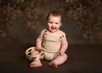 Fine-Art styled portrait of a baby boy in a brown knit romper against an autumnal backdrop, photograph by Christchurch Baby Photographer Kirsten Naomi Photography