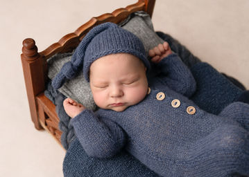 Newborn baby boy wearing a knitted blue romper and hat in a relaxed sleep on a tiny bed by Christchurch newborn baby & family photographer Kirsten Naomi Photography