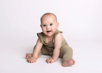 Baby girl in green knit overalls sitting up during a milestone portrait session by Christchurch baby photographer Kirsten Naomi Photography