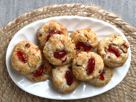 white oval plate on a straw mat. The plate holds rounded cookies coated with crushed corn flakes cereal and a slice of maraschino cherry on top