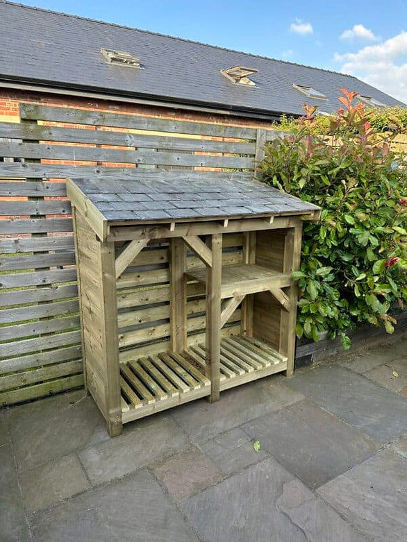 Thumbnail: small log store with kindling shelf and slate roof with fence behind