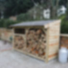 handmade log store with a reclaimed slate roof filled with logs side angle view