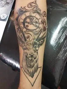 Tatouage complexe d'une tête de Cerf qui tient entre ses bois une horloge détaillées sur l'avant bras