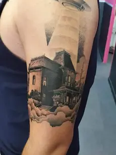 Tatouage architectural réaliste sur bras, représentant la maison du film "Psychose", réalisé en noir et gris. Une composition très précise par Patrick à Quissac.