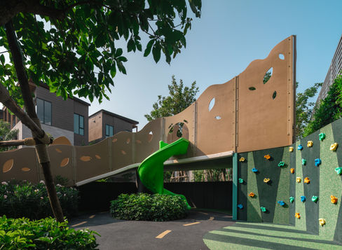 View of Vana Tree House Playground at Vana Residence showing the treehouse structure, curved slide, and small climbing wall designed by VV Desine.