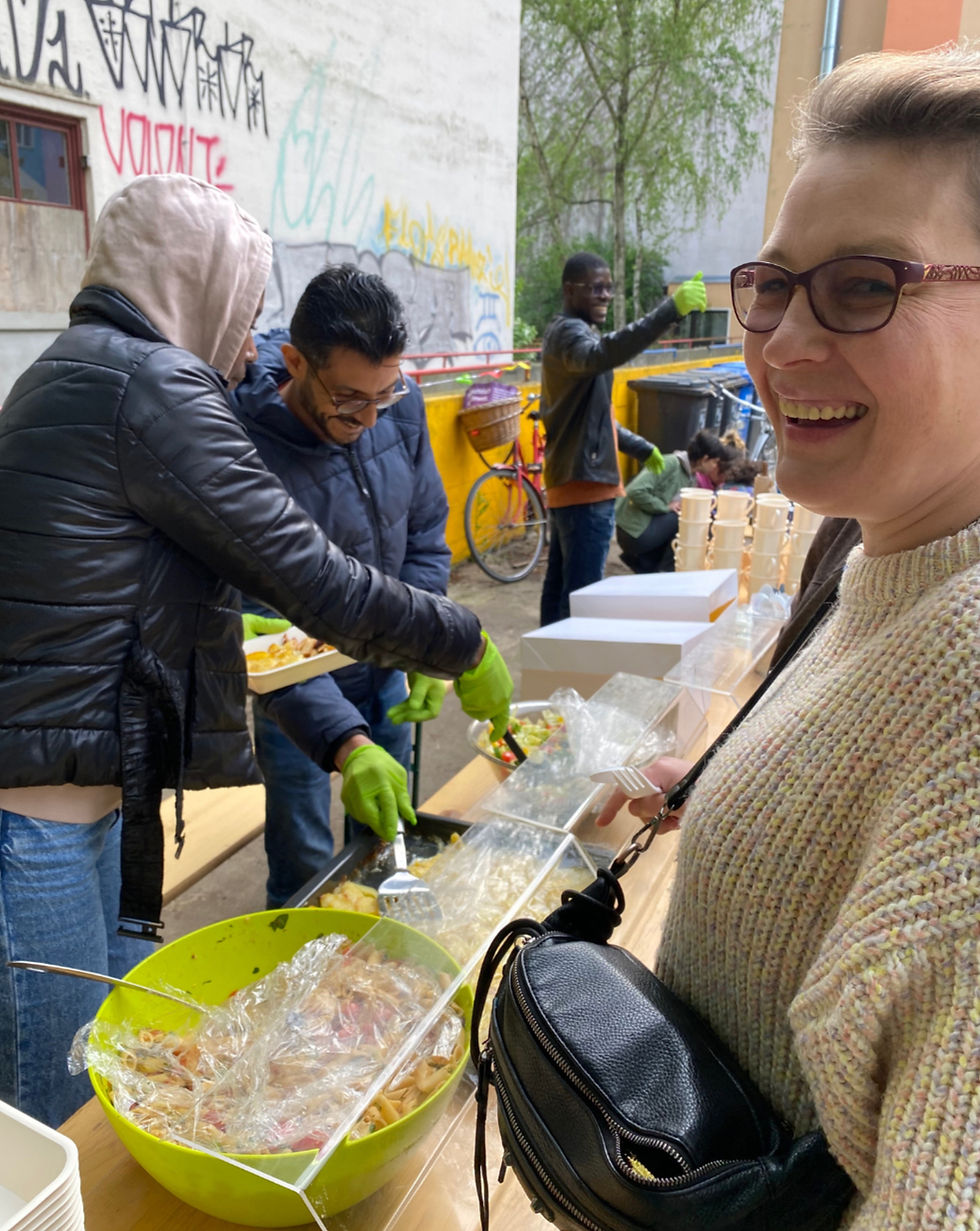 Menschen bereiten Essen vor, Kiezbegegnung mit lächelnder Frau und anderen Personen.