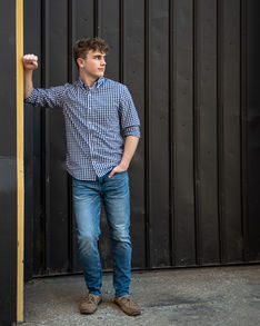 Young man in a button-down shirt and jeans in an urban setting.