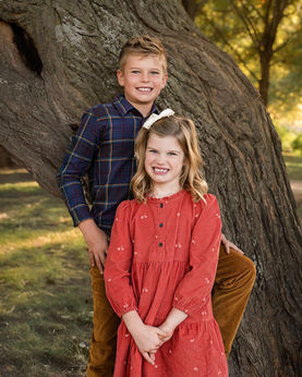Brother and sister smiling for family portraits by a tree