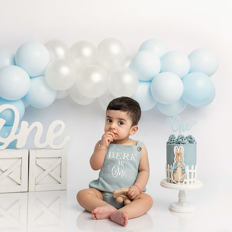 First birthday portrait. Boy sitting next to birthday cake. Blue and white balloon garland.  Peter Rabbit Cake Smash Theme. First birthday photos by cake smash photographer in march Cambridgeshire