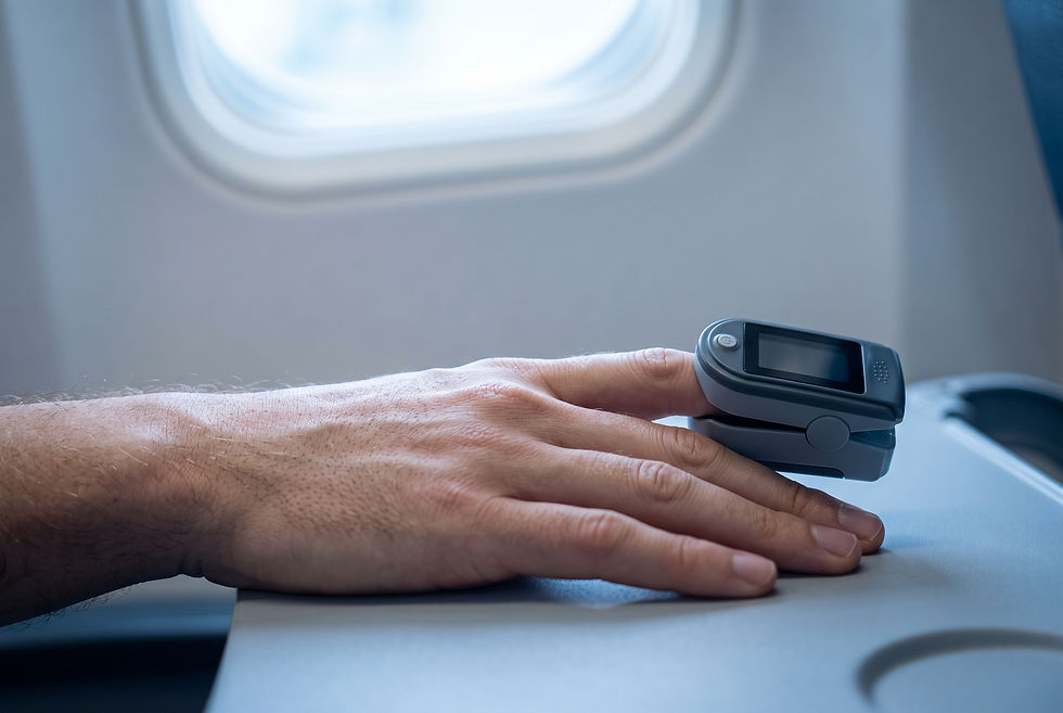 Fingertip pulse oximeter clipped to a hand resting on an airline tray table, with a cabin window in the background