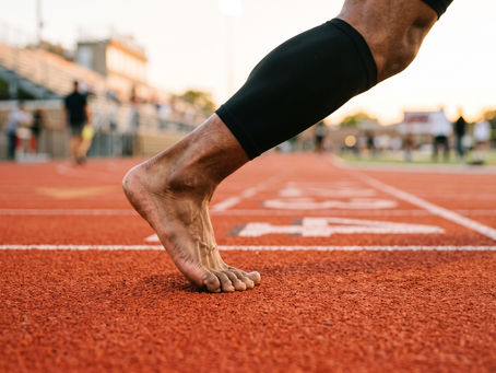 Close-up of a sprinter's bare foot at the instant of push-off on a running track, weight driving through the forefoot and big toe.