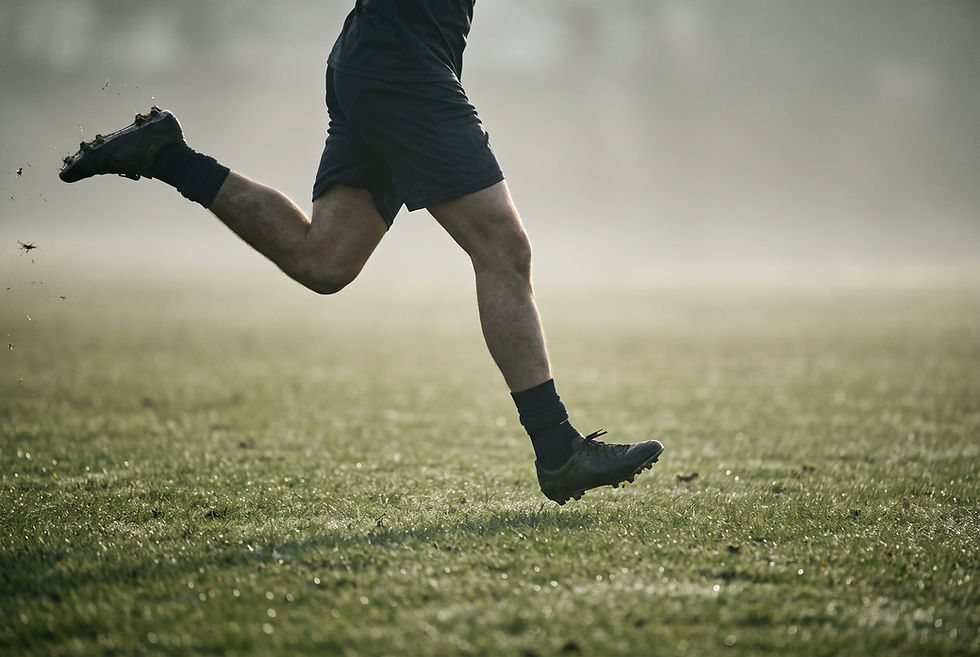 Footballer sprinting on a grass pitch, shown from the hip down, with the swing leg extending forward just before foot contact.