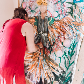 Kvinna o röd klänning målar stort färgglatt konstverk mot ljusa väggar på Hälsans Hus. 