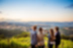 Four friends toast with red wine in a vineyard at sunset, overlooking rolling mountains and a pastel sky.