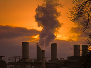 Industrial smokestacks emitting Scope 1 emissions at sunset, representing direct greenhouse gas emissions from manufacturing facilities