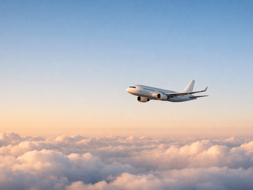 A commercial airplane flying above a layer of soft clouds during golden hour, with a clear sky and warm light on the horizon.