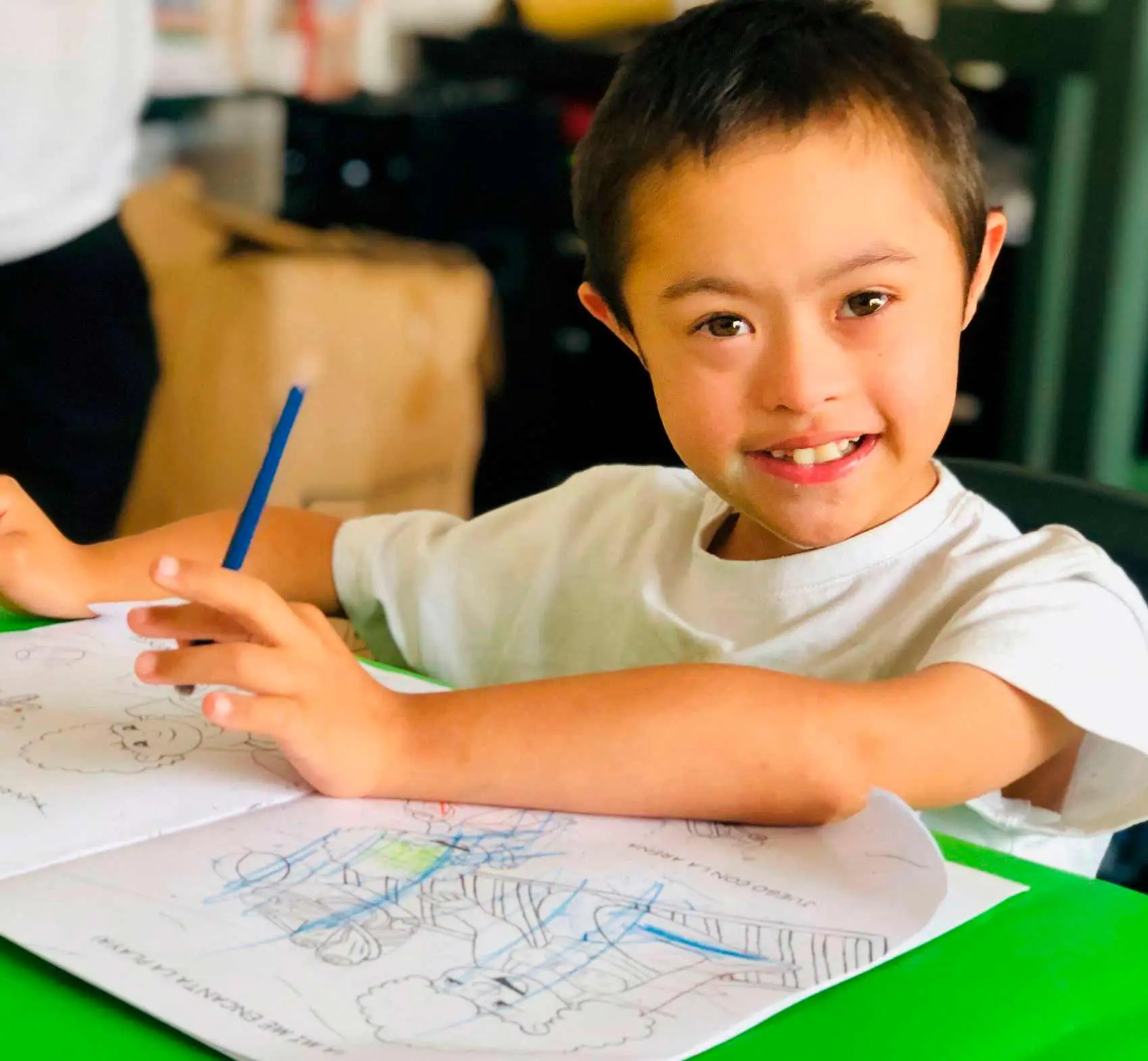 Estudiante con síndrome de down sonriendo mientras trabaja sobre un libro de pintar