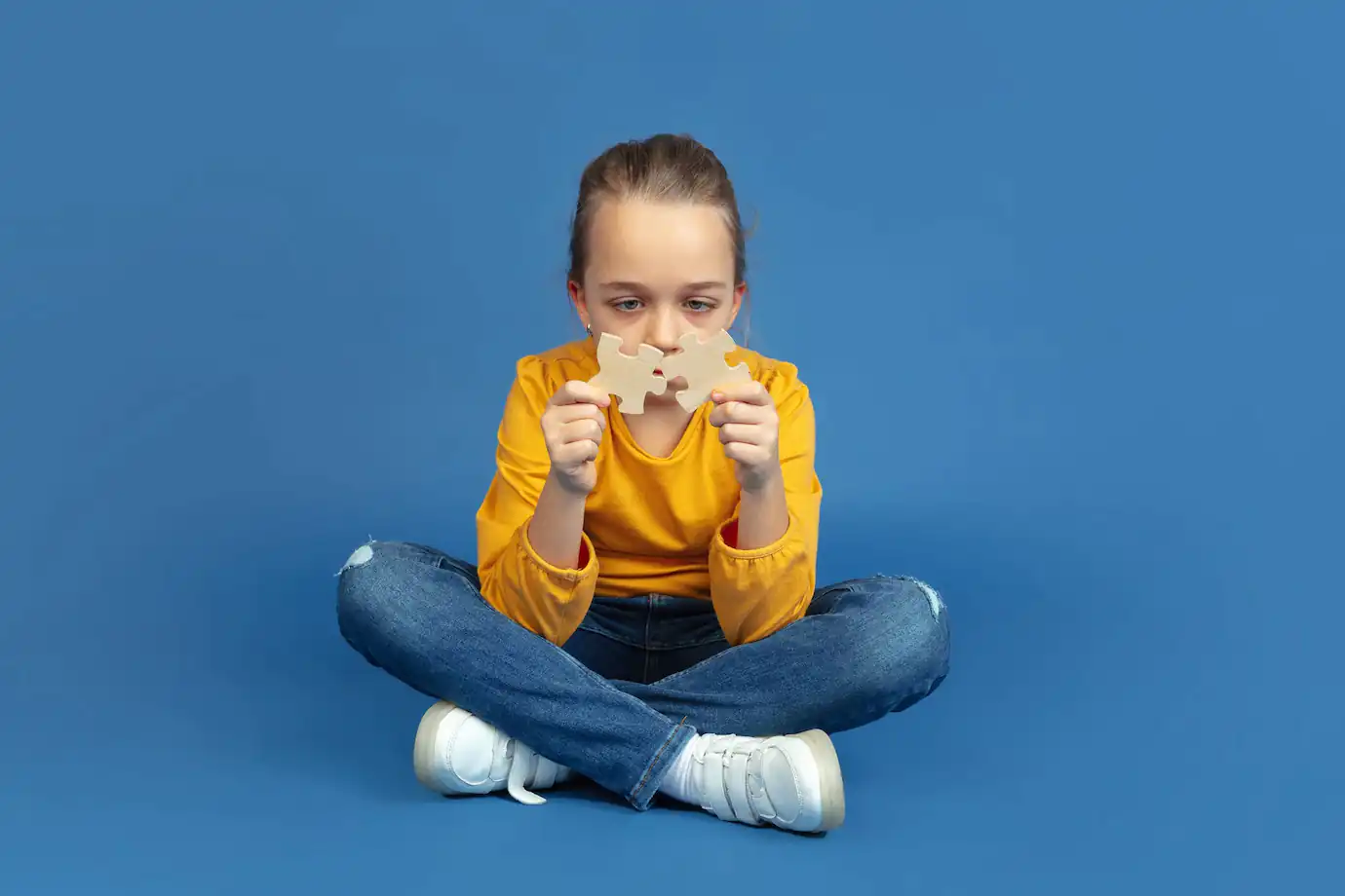 Niña con autismo de buzo amarillo mirando las piezas de un puzle.