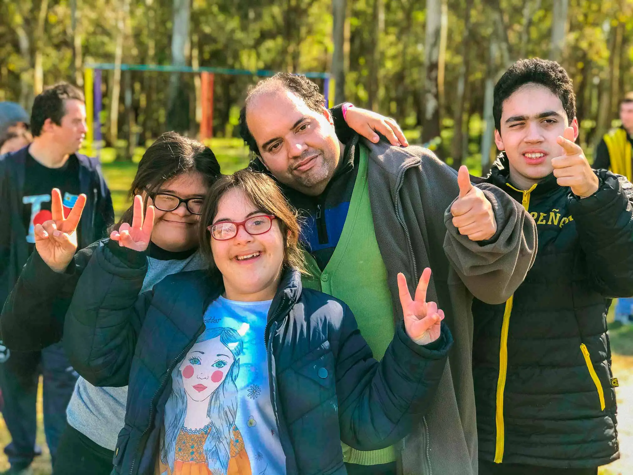 Personas con síndrome de down y discapacidad intelectual abrazadas, sonriendo y levantando los dedos