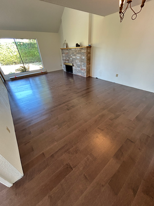 Living room featuring hardwood flooring, a stone fireplace, and large windows.