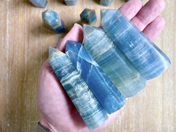 Four radiant Celestite Obelisk Points, also known as Blue Calcite Quartz, displayed in hand, showcasing their elegant translucent blue hues.