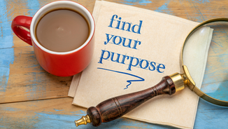 Red coffee cup, napkin with "find your purpose" in blue, and magnifying glass on a wooden table. Vibrant and thoughtful atmosphere.