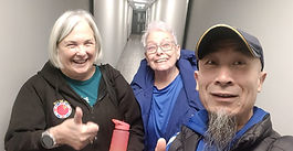 Two women and their Tai Chi instructor smiling in a hallway while taking a selfie, giving thumbs up.