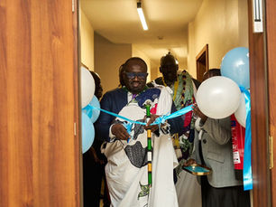 Hon. Rizig Dominic Samuel, the new General Director of the NCA, ceremonially cuts the ribbon as he assumes office, surrounded by colleagues and celebratory decorations.