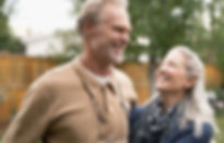 Pareja mayor sonriente disfrutando de una conversación al aire libre, destacando la importancia de una buena audición y el uso de aparatos auditivos para mejorar la calidad de vida.