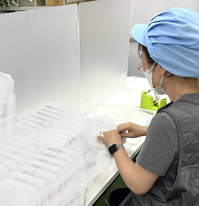 プライドの請け負う100均商品の梱包作業。衛生面を考慮し、作業キャップとマスクは必須。個別に作業し、流れ作業はしないシステム。