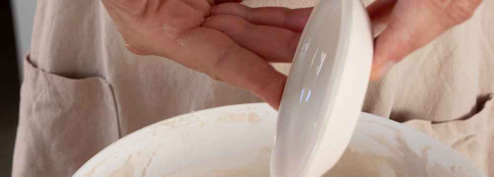 Eine Frau dreht auf der Töpferscheibe eine kleine Schale und verfeinert sie mit der Gumminiere.