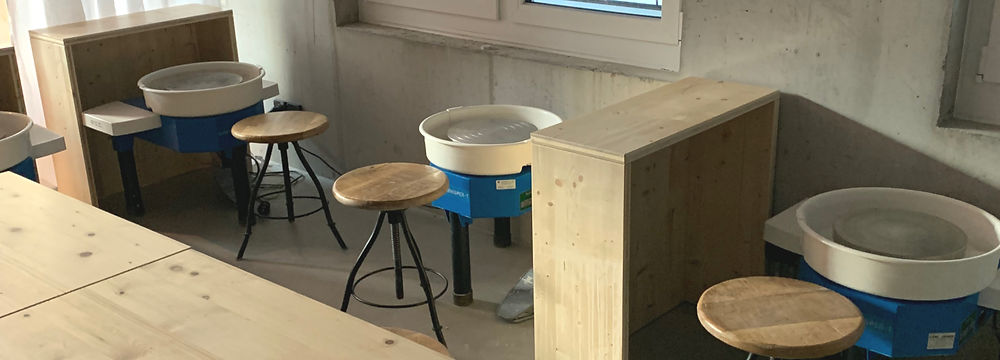 Eine Frau dreht auf der Töpferscheibe eine kleine Schale und verfeinert sie mit der Gumminiere.