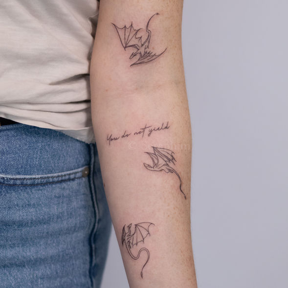 Small fineline three dragon tattoo and script in delicate black and grey, featuring a quote from Throne of Glass book, created by Seraphim in Seattle, WA.