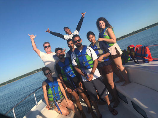 Group of friends in life vests posing on a boat with a clear blue sky.