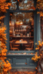 Cafe window view with warm lighting, wooden chairs, and a menu inside. Framed by vivid orange autumn leaves, creating a cozy ambiance.