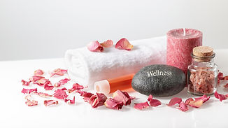 Wellness decoration with bottle of salt, dried rose petals and engraved stone on light bac