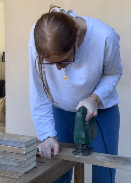 femme entrain de scier à la scie sauteuse une latte de palette de bois