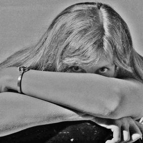 Person with long hair resting head on folded arms, eyes peeking out