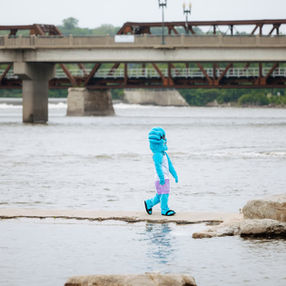 Person dressed in a blue wave mascot costume walking along a fishing jetty
